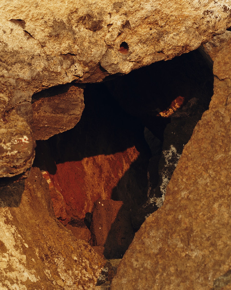 A close-up photograph of a small cave in rock tinted orange and red at Fort Rock in Oregon.